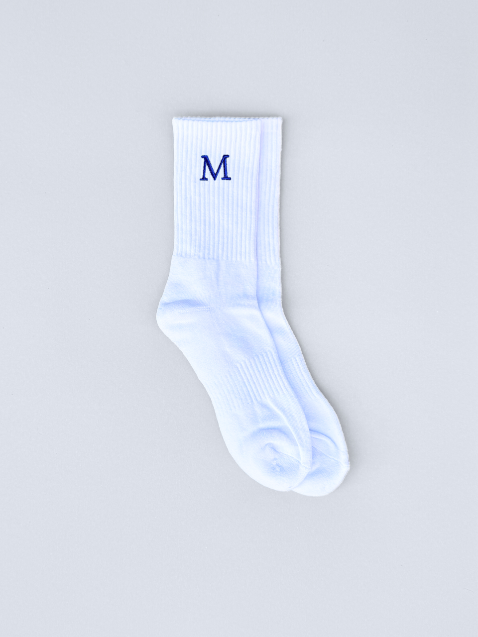 Weiße Socken mit gestickter Initiale M, flach ausgebreitet
